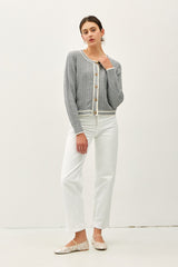 A front-facing, full-body view of a model wearing the grey cable knit cardigan to showcase its fit and length. She looks at the camera with one hand near her neckline.