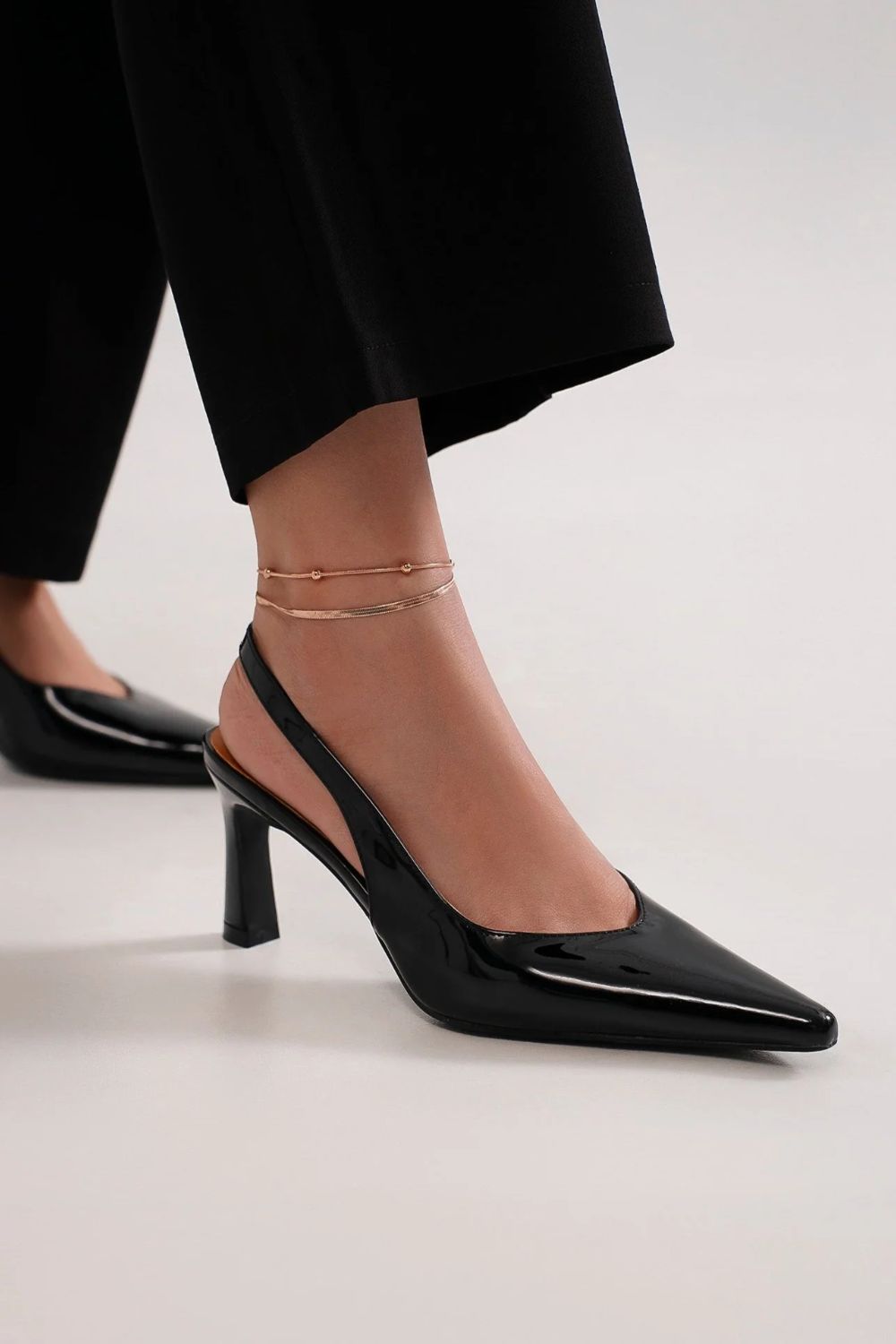Black faux leather point toe slingback pumps showcased with chic ankle accessories, perfect for stylish outings.