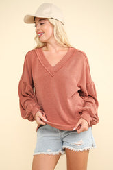 Woman wearing a two-tone ribbed V-neck top with oversized sleeves and a cap, styled with denim shorts. Perfect for autumn.