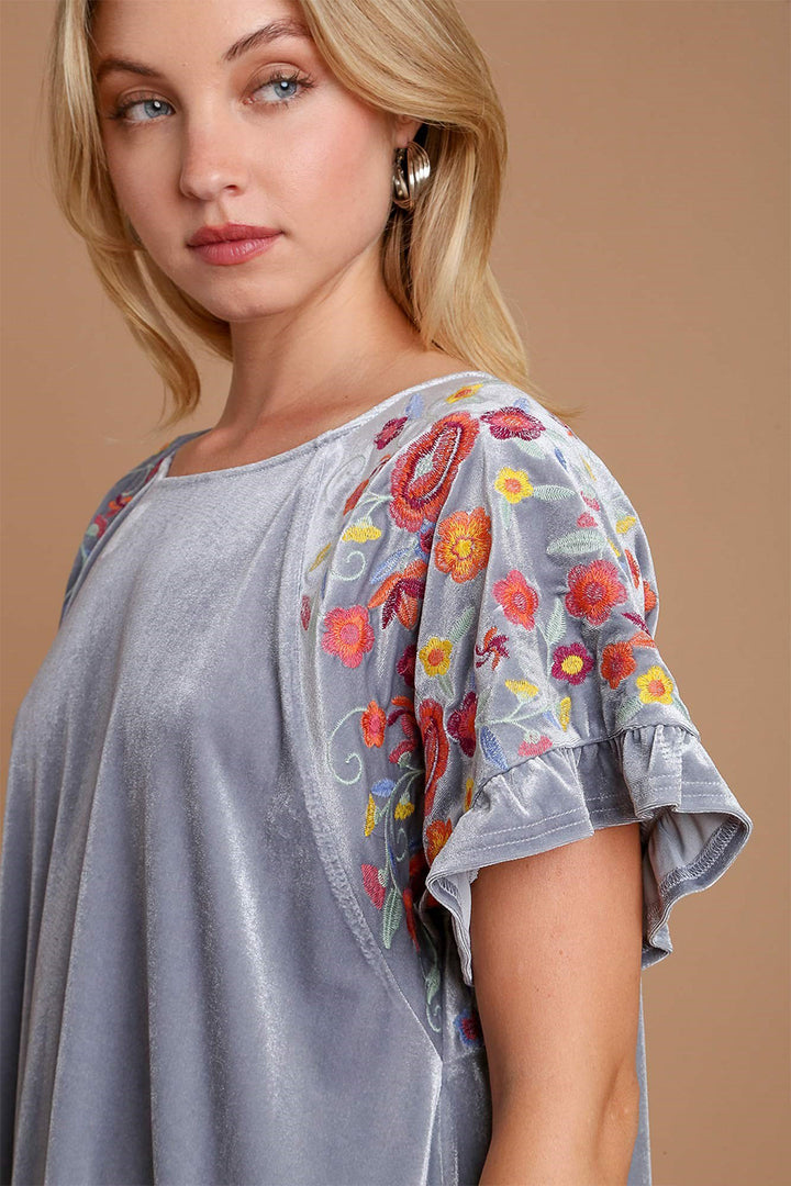 Model wearing Umgee Velvet Embroidery Short Sleeve Blouse with colorful floral embroidery on a soft velvety fabric.