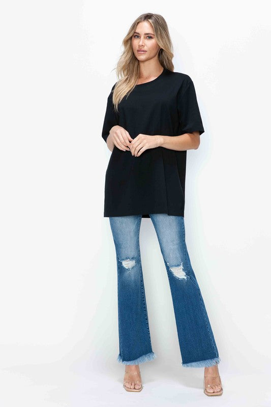 Woman wearing black oversized t-shirt with bytos distressed high rise bootcut jeans and heels, showcasing trendy casual style.