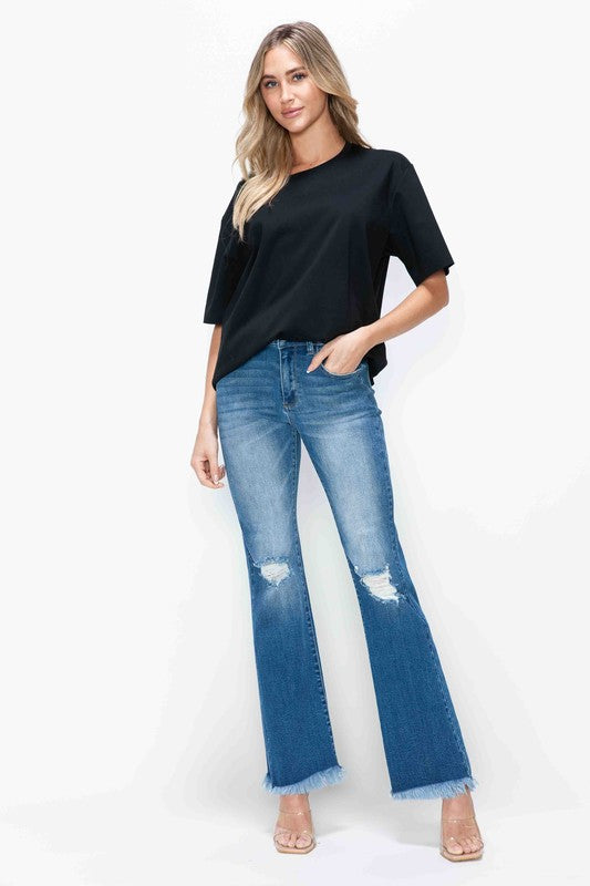 Woman wearing bytos distressed high rise bootcut jeans with raw hem, paired with a black top and heels.