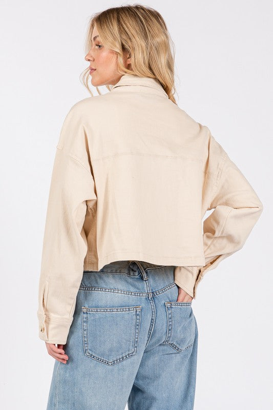 Woman wearing a cropped beige jacket from the back, featuring a relaxed fit and stylish buttoned cuffs.