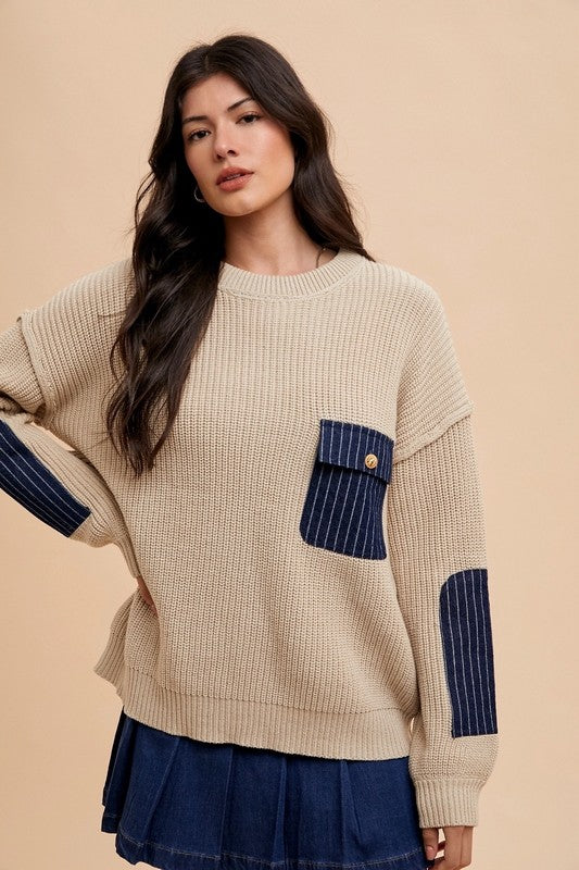 Woman wearing a beige contrast round neck drop shoulder sweater with patch pocket and denim skirt against a neutral background.