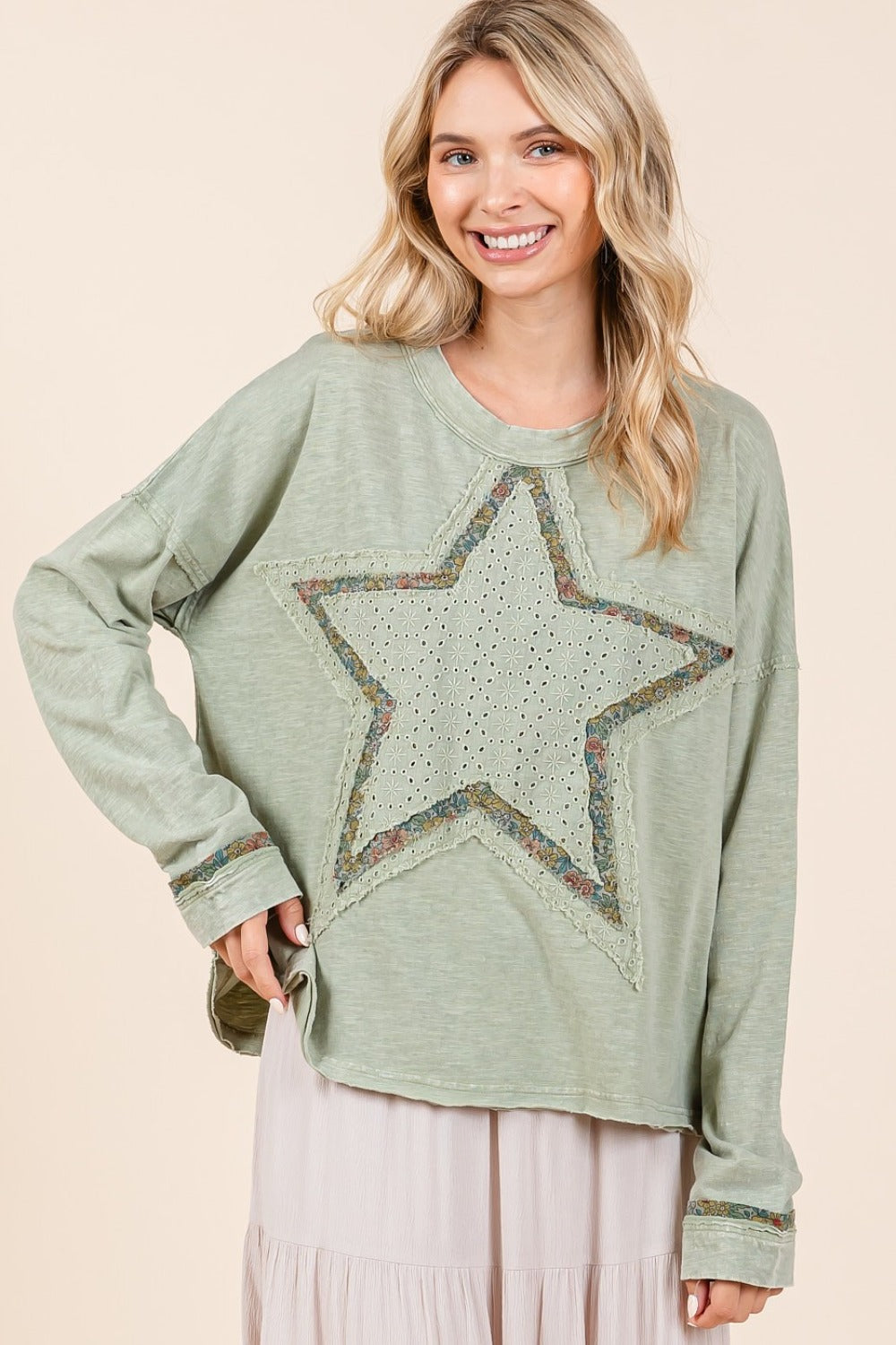 A Smiling woman wearing a green long sleeve t-shirt with a star patch