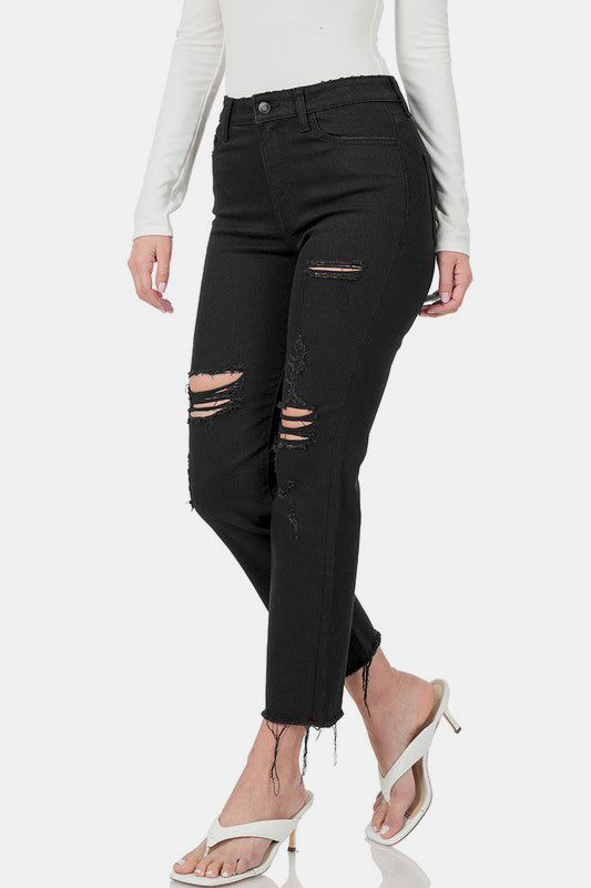 Distressed black cropped jeans with raw hem, styled with a white top and open-toe heels, showcasing a trendy casual look.