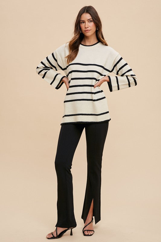 Model wearing Annie Wear side slit striped round neck sweater with black pants and heels against a neutral background.