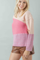 A Side shot of the model who is smiling wearing the color-blocked sweater to illustrate its profile and fit over brown leather-look shorts. The image clearly shows the contrasting knit textures.
