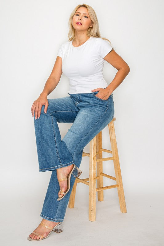 Woman seated on a stool wearing bytos Cat's Whiskers Mid Rise Bootcut Jeans and a white t-shirt, showcasing a stylish look.