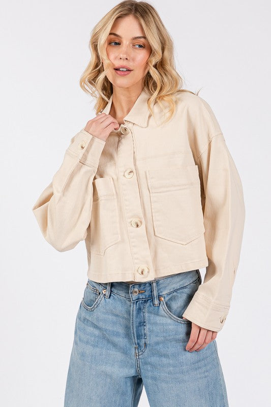 Woman wearing a cropped beige button-down denim jacket with patch pockets, paired with light blue jeans.