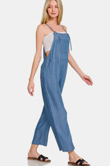 Woman wearing washed adjustable strap wide leg denim overalls, styled casually with a tank top and sandals.