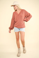 Model wearing a two-tone ribbed V-neck oversized top with denim shorts and boots, perfect for early autumn style.