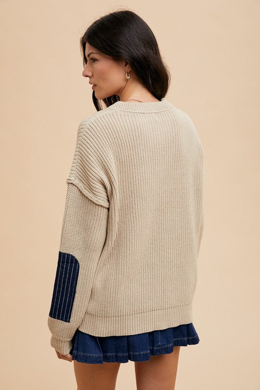 Woman wearing a beige contrast round neck drop shoulder sweater with patch pocket, showcasing a relaxed fit from the back.